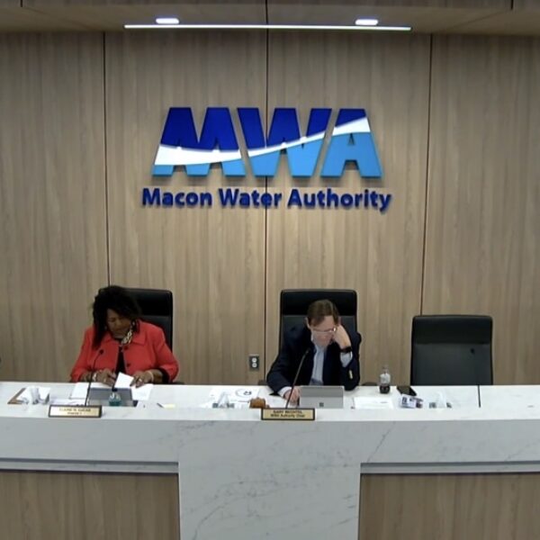 Six people sit at a long conference table under a sign reading Macon Water Authority, reviewing papers in a wood-paneled room.