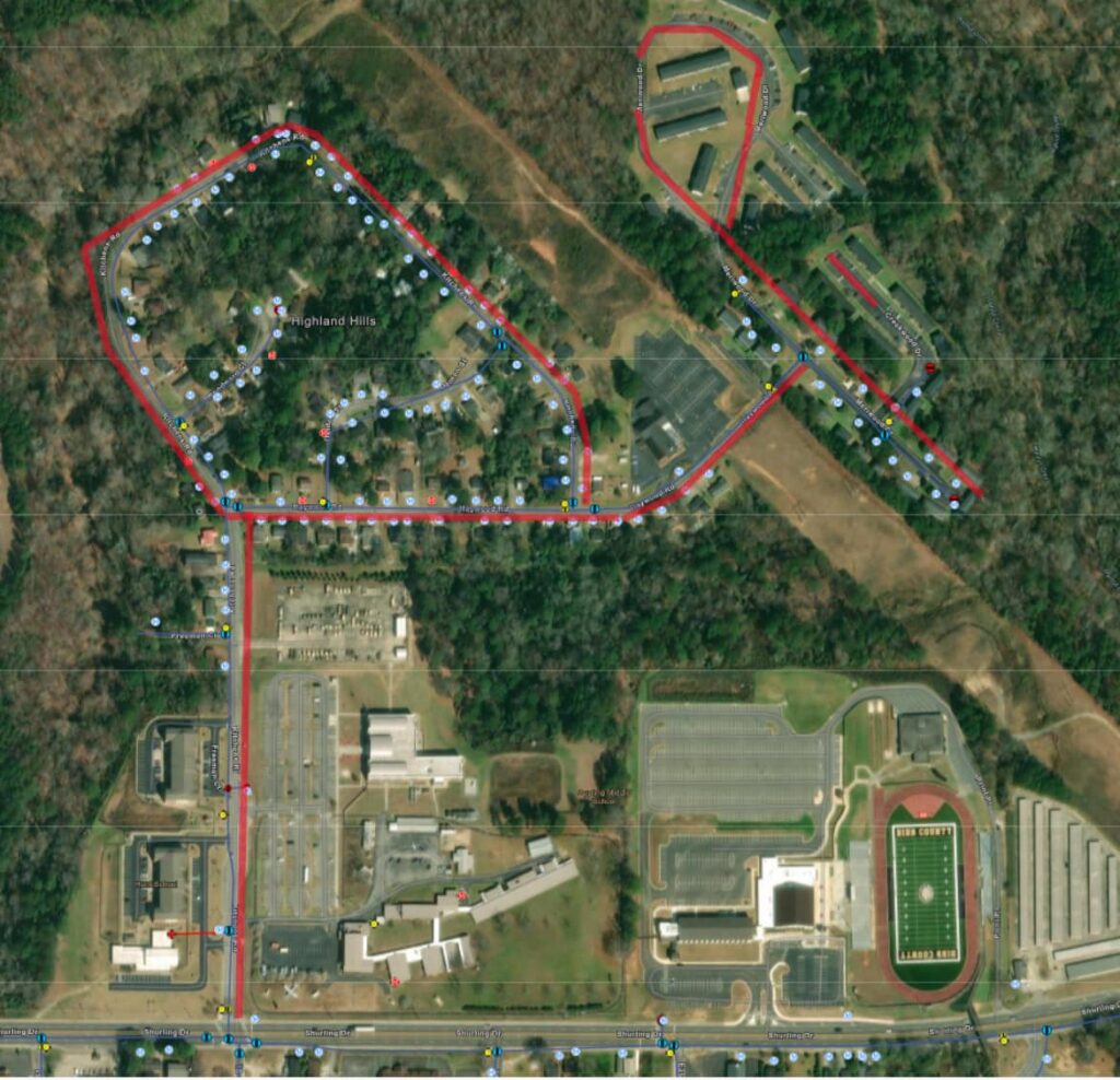 Aerial view of a neighborhood with parking lots, buildings, and stadium; a red route line weaves through roads and green spaces.