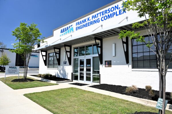 Front entrance of the Frank K. Patterson Engineering Complex, modern white building with large windows, sign above door, trimmed grass, small trees.