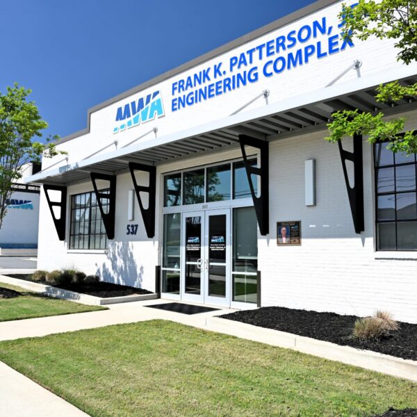 Front entrance of the Frank K. Patterson Engineering Complex, modern white building with large windows, sign above door, trimmed grass, small trees.