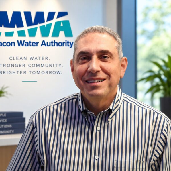 A man in a striped shirt smiles in an office with Macon Water Authority signage. Text reads: Michel Wanna, Executive Director & President. Slogan: Clean water. Stronger community. Brighter tomorrow.