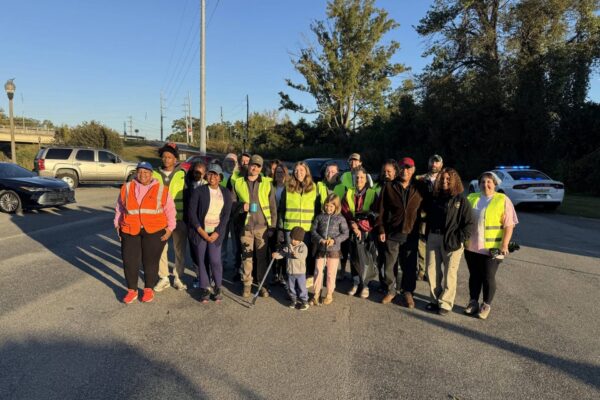 A group of volunteers in neon safety vests pose together in a parking lot, some holding litter grabbers.