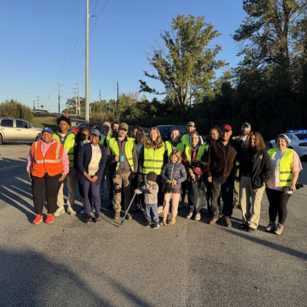 A group of volunteers in neon safety vests pose together in a parking lot, some holding litter grabbers.